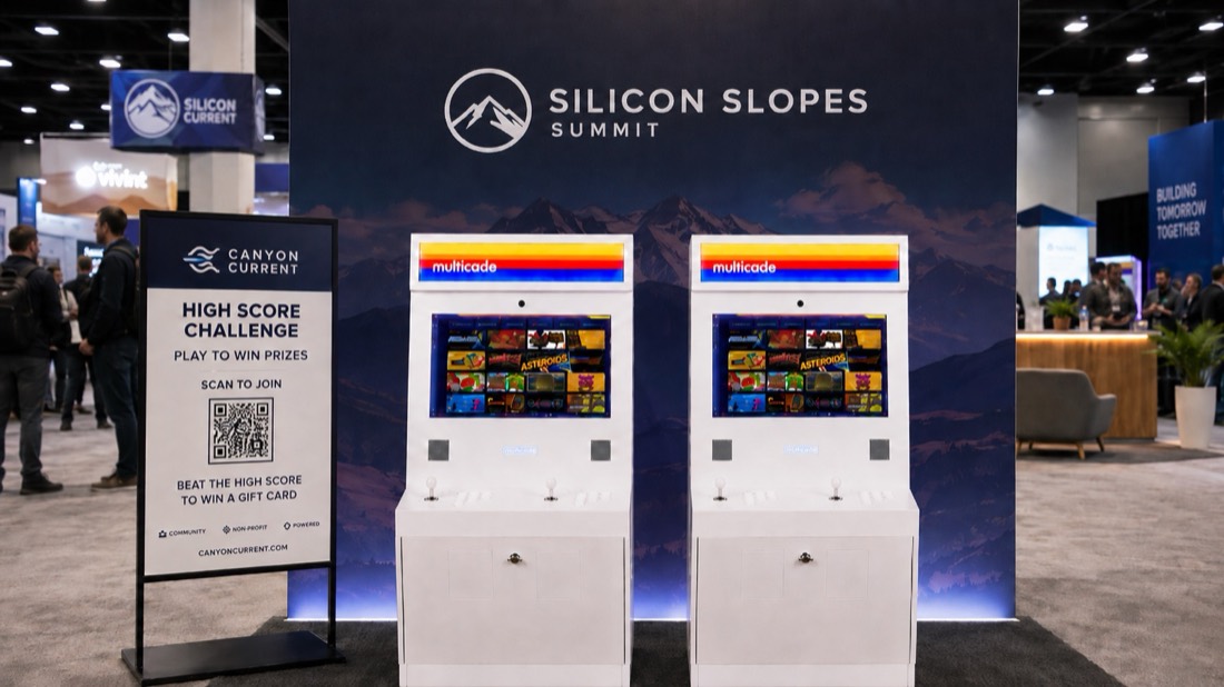 Two branded multicade arcade machines at a Silicon Slopes Summit trade show booth with a High Score Challenge sign and QR code.